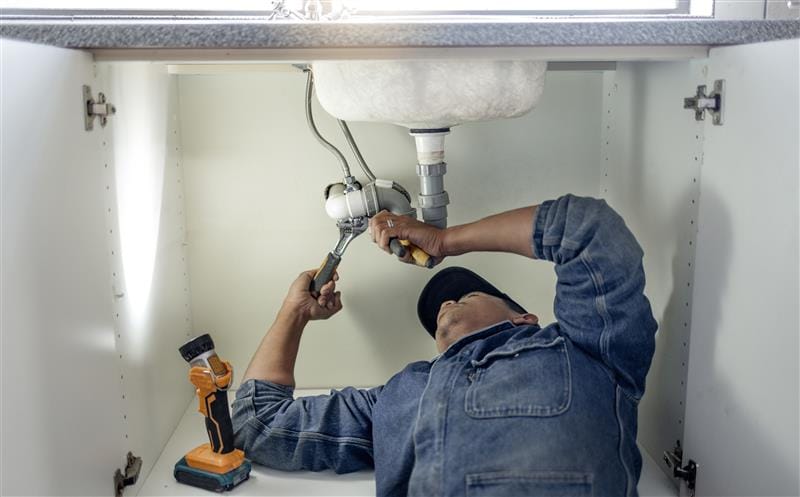 Plumber repairing pipes beneath a bathroom sink in Coconut Creek