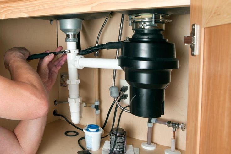 Plumber installing a garbage disposal beneath a kitchen sink in Coconut Creek