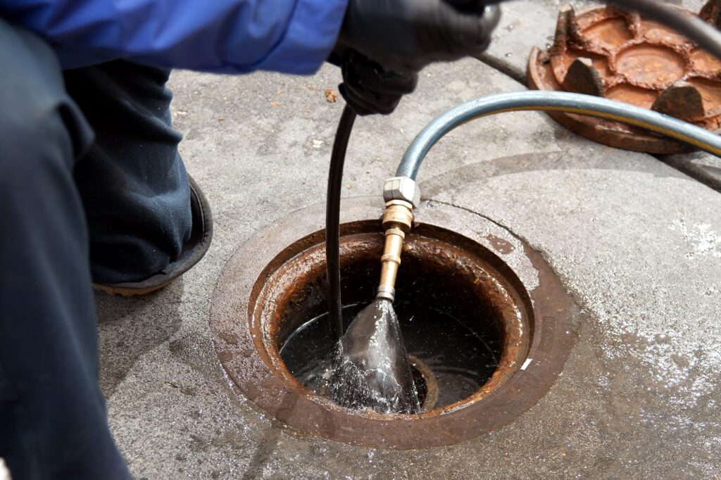 Plumber hydro jetting a sewer line through a manhole in Coconut Creek