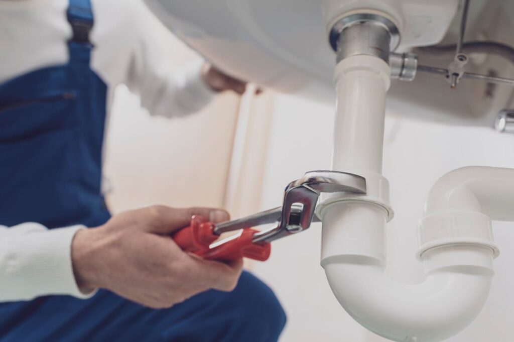 Plumber repairing a white drain pipe beneath a sink in Coconut Creek
