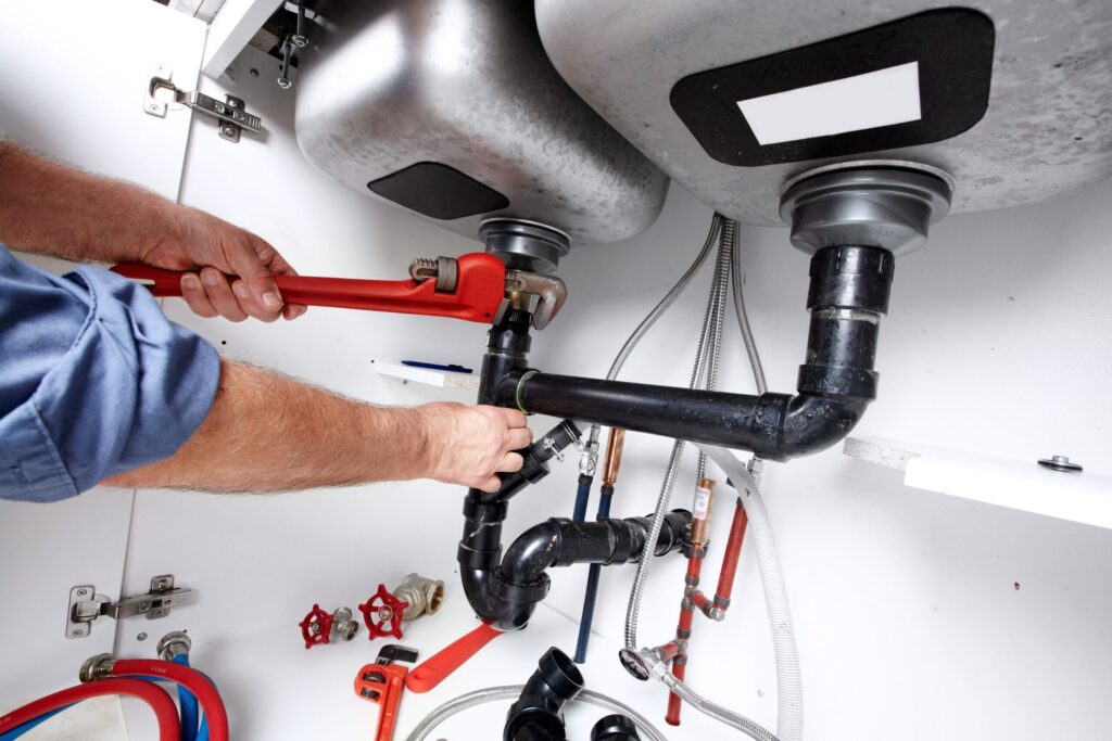 Plumber repairing drain pipes beneath a kitchen sink in Coconut Creek