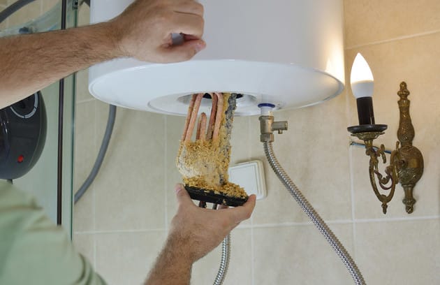 Technician removing mineral buildup from a water heater in Coconut Creek